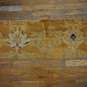 Mustard yellow, high-pile rug with navy and beige floral patterns lying on distressed wood planks.