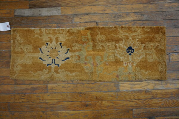Mustard yellow, high-pile rug with navy and beige floral patterns lying on distressed wood planks.