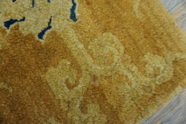 A close-up view of a high-pile gold and brown rug with navy accents resting on gray wood flooring.