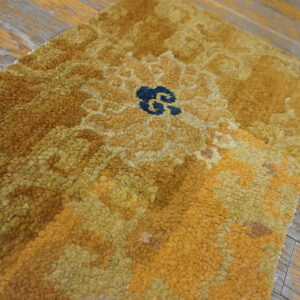 Close-up of a high-pile gold and brown rug featuring a central blue motif on worn wooden planks.