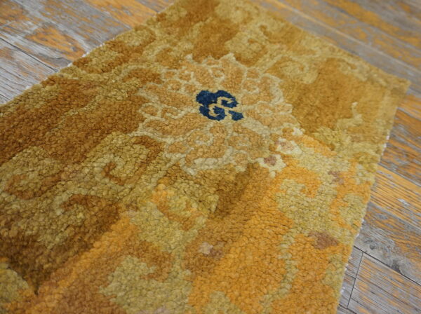 Close-up of a high-pile gold and brown rug featuring a central blue motif on worn wooden planks.