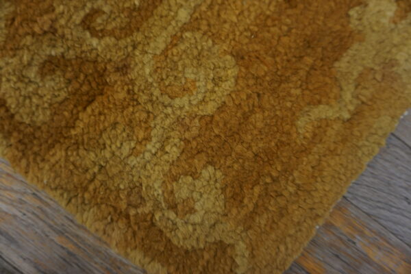 A shaggy, looped gold rug corner displays an amber tonal pattern against gray wood flooring.