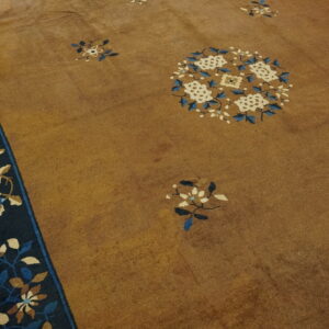 Golden brown rug with blue and cream floral patterns and a dark border rests on plank wood flooring.