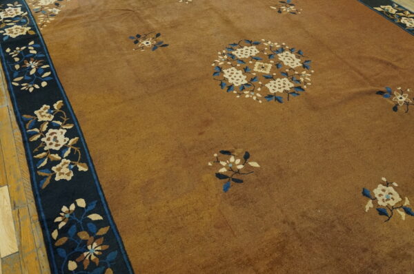 Golden brown rug with blue and cream floral patterns and a dark border rests on plank wood flooring.