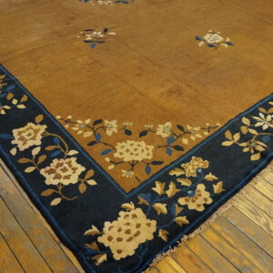 Mustard rug corner shows a navy blue border with beige and blue floral patterns on wood floors.
