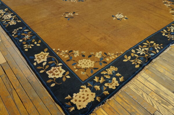 Mustard rug corner shows a navy blue border with beige and blue floral patterns on wood floors.