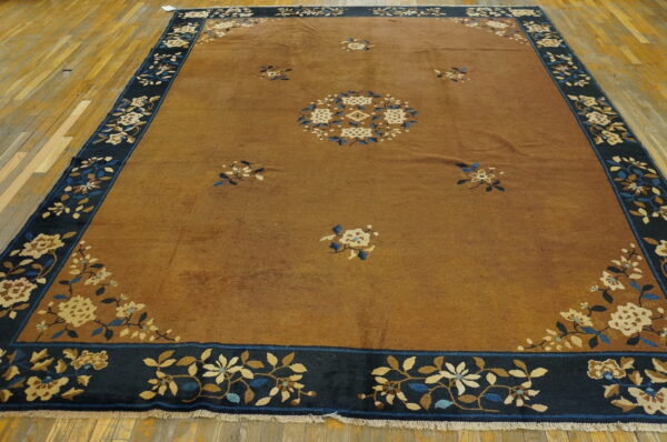 Golden brown rug with a navy blue border featuring cream and blue floral patterns on wood floors.