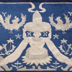 Low-pile blue rug with a beige design featuring two snarling beasts flanking a central figure.