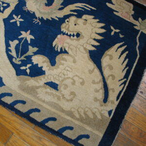 Dark blue rug with beige dragon and floral patterns rests on distressed wood flooring.