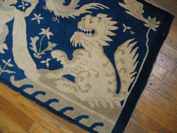 Dark blue rug with beige dragon and floral patterns rests on distressed wood flooring.