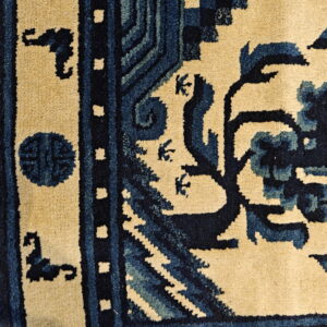 Cream and navy blue rug detail showing an ornate border and stylized floral patterns on a tan field.
