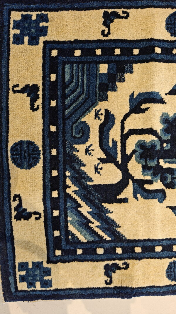 Cream and navy blue rug detail showing an ornate border and stylized floral patterns on a tan field.
