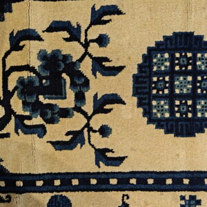Short-pile tan rug with bold dark blue floral and geometric patterns rests on light square tiles.