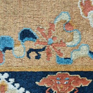 Textured pile rug detail in rust, cream, and blue against a tan field and a navy blue border.