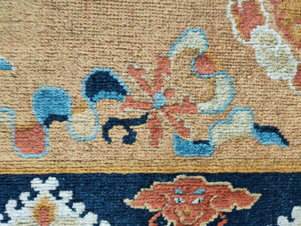Textured pile rug detail in rust, cream, and blue against a tan field and a navy blue border.