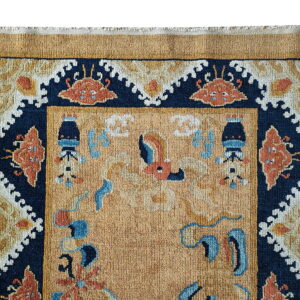 Detail of a gold rug showing the navy border with terracotta and cream traditional designs.