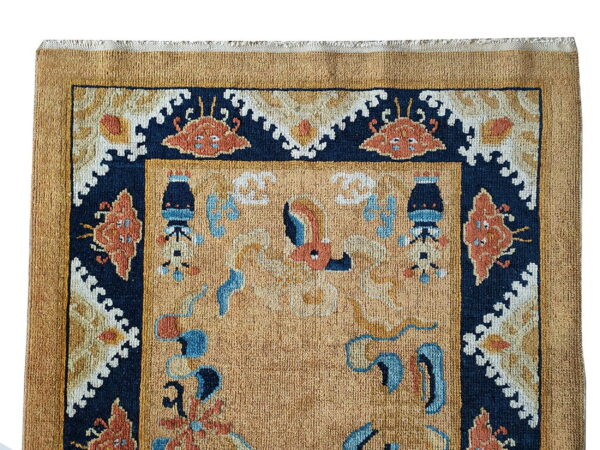 Detail of a gold rug showing the navy border with terracotta and cream traditional designs.