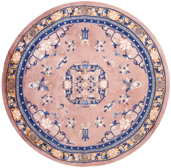 Round dusty rose rug with elaborate blue, apricot, and white stylized floral and geometric patterns.