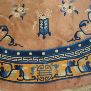 Close-up of a round dusty rose rug featuring blue floral motifs and an orange, blue, and white geometric border.