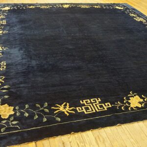 Dark blue rug featuring a low pile and a gold floral and geometric border on hardwood flooring.