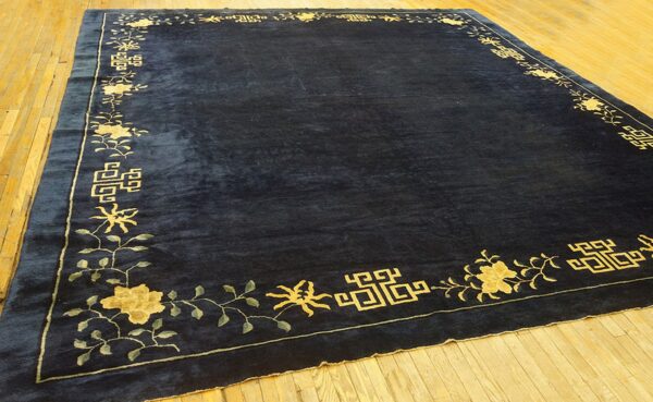Dark blue rug featuring a low pile and a gold floral and geometric border on hardwood flooring.