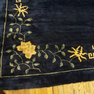 Deep blue high-pile rug displaying a gold floral vine and geometric pattern border on rustic wood floors.