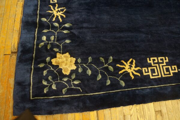 Deep blue high-pile rug displaying a gold floral vine and geometric pattern border on rustic wood floors.
