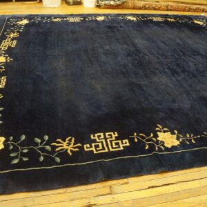 Rectangular navy rug featuring a gold floral and fretwork border on light hardwood floors.