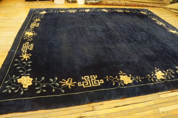 Rectangular navy rug featuring a gold floral and fretwork border on light hardwood floors.