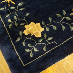 Dark blue plush rug corner with a yellow floral pattern and green vines on golden wood planks.