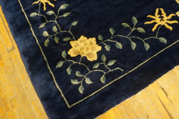 Dark blue plush rug corner with a yellow floral pattern and green vines on golden wood planks.