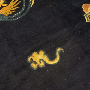 Close-up of a dark navy rug featuring stylized golden yellow and teal dragon and cloud motifs.