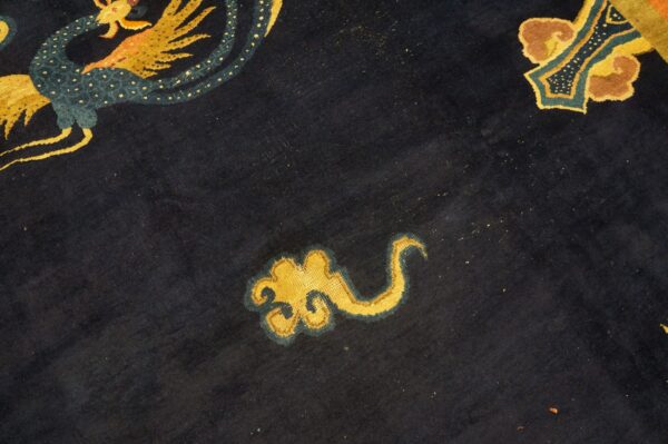 Close-up of a dark navy rug featuring stylized golden yellow and teal dragon and cloud motifs.