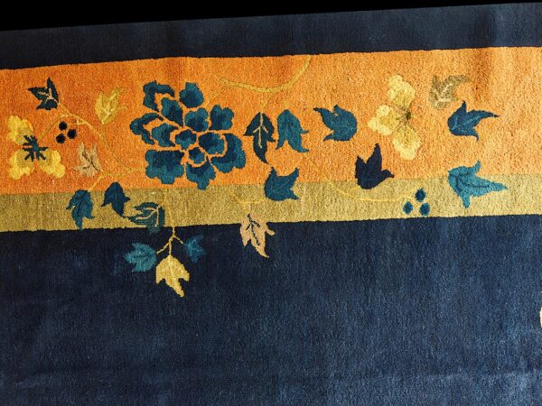 Textured navy rug with a bright orange band featuring teal and yellow stylized floral patterns.