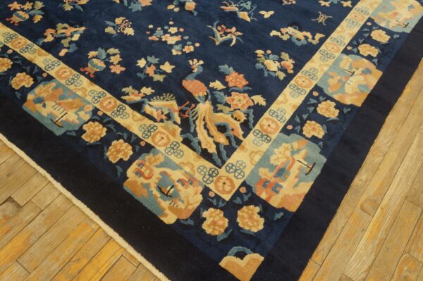 Dark blue traditional rug with gold, peach, and teal floral patterns rests on light wood parquet flooring.