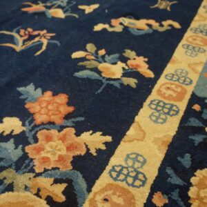 Navy rug with plush pile features coral and gold floral pattern separated by a light yellow geometric border.