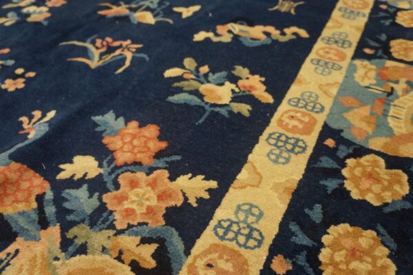 Navy rug with plush pile features coral and gold floral pattern separated by a light yellow geometric border.