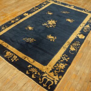 Deep blue rug with gold floral patterns and thick borders rests on distressed light wood flooring.