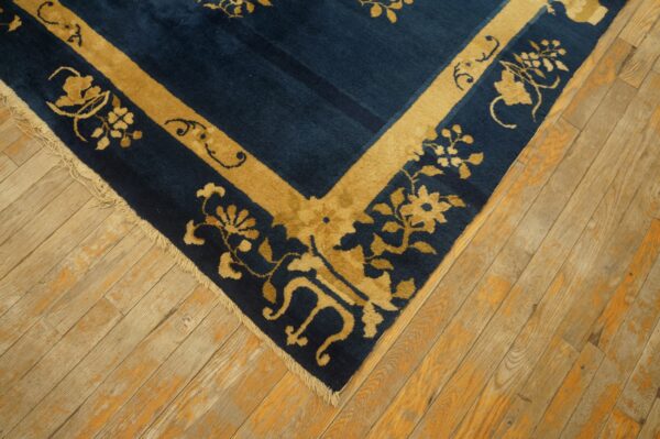 Dark blue rug with tan floral motifs and a gold border detail rests on worn hardwood flooring.