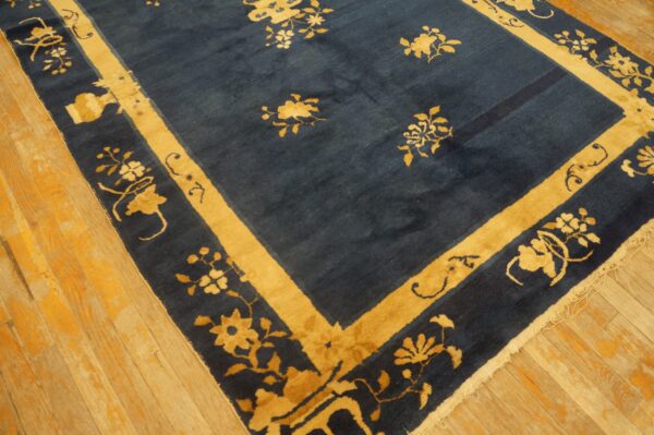 A navy rug with medium pile features scattered gold floral motifs and a wide gold border on wood planks.