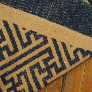 Tan flatweave rug with navy blue geometric patterns folded on distressed amber wood planks.
