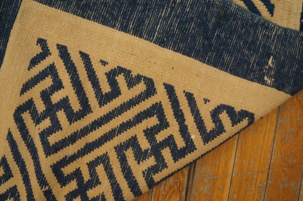 Tan flatweave rug with navy blue geometric patterns folded on distressed amber wood planks.