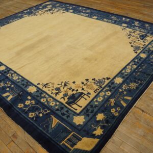 Square cream and deep blue bordered rug with floral and scenic patterns sits upon distressed hardwood floors.