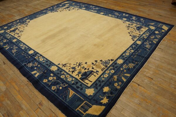 Square cream and deep blue bordered rug with floral and scenic patterns sits upon distressed hardwood floors.