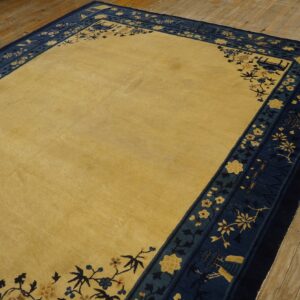 Low-pile rug with a solid gold field and detailed navy and gold floral border on rustic wood planks.
