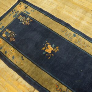Navy blue hallway runner rug with gold and blue floral borders lies on distressed wood plank flooring.
