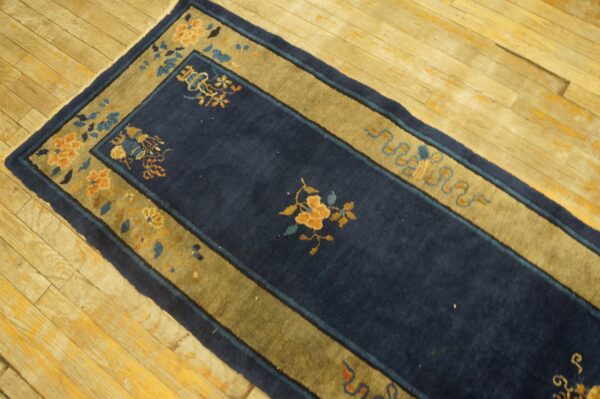Navy blue hallway runner rug with gold and blue floral borders lies on distressed wood plank flooring.