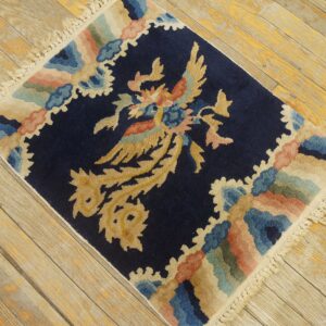 Navy blue rug with a central gold bird design and multicolored scalloped border on worn wooden floorboards.