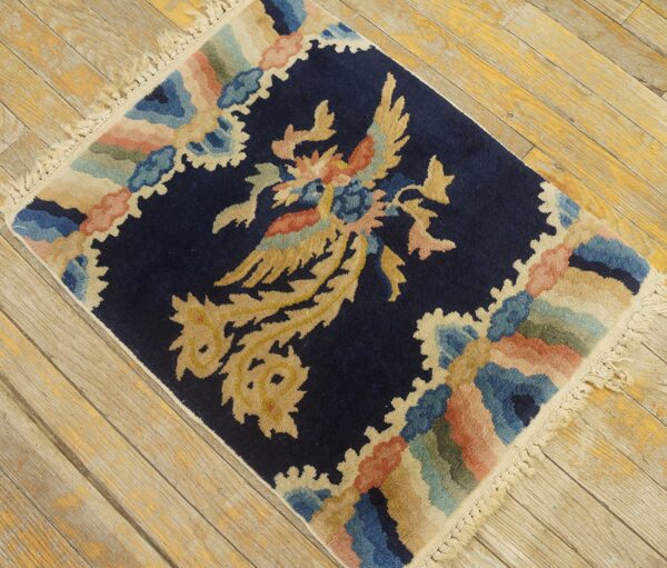 Navy blue rug with a central gold bird design and multicolored scalloped border on worn wooden floorboards.