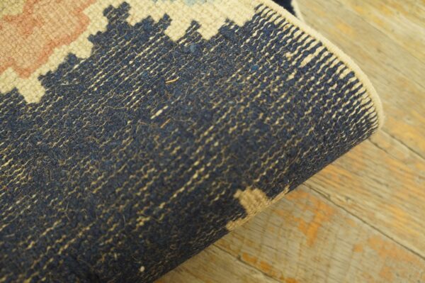 The rolled edge of a pink, cream, and navy rug reveals its ribbed backing on distressed wood floors.